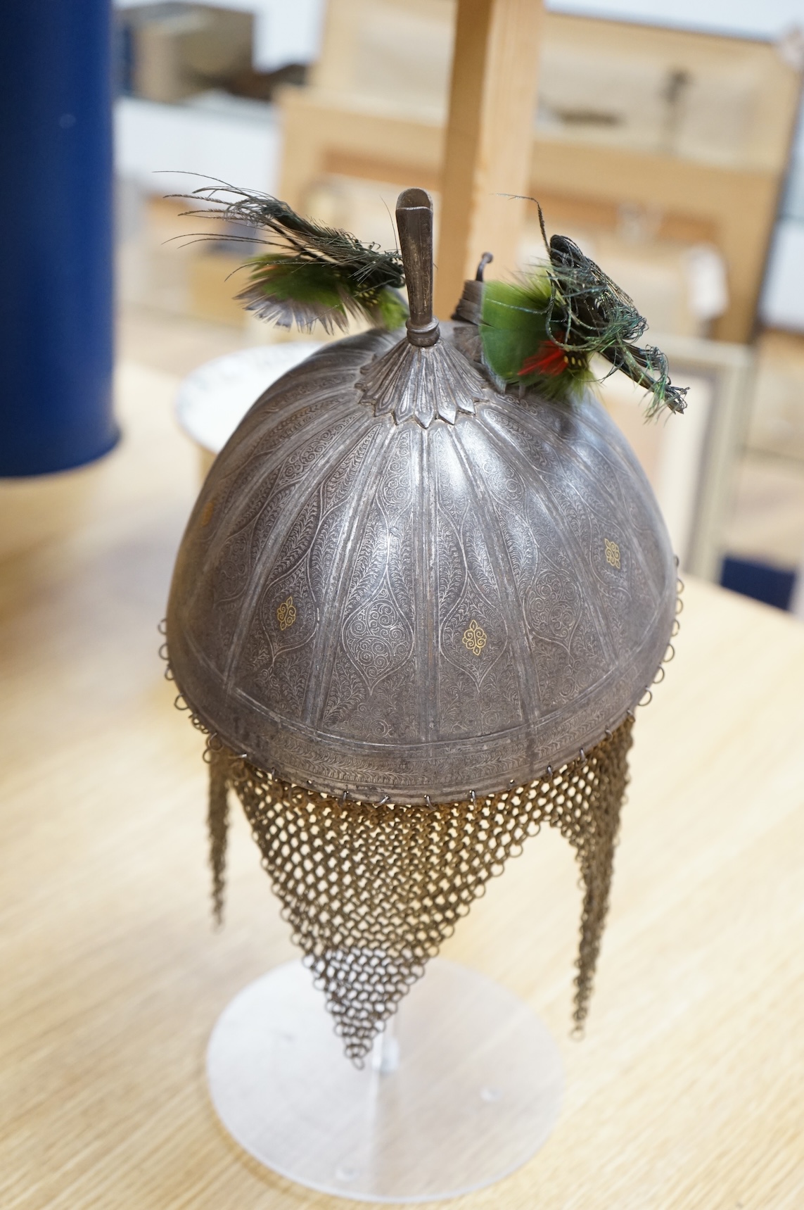 A mid to late 19th century Indian helmet and matching shield, covered with silver koftgari decoration, the helmet with sliding nasal bar and twin plume sockets surmounted by a third plume socket, the skull fluted like a